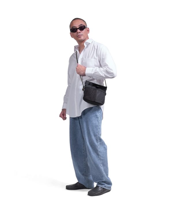 Male model in relaxed urban streetwear wearing the black SYMA Chain crossbody, demonstrating its ultra-lightweight and minimalist scale. Compact sacoche bag.