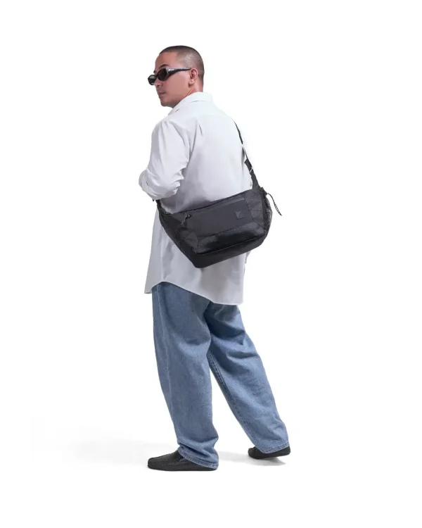 Male model in relaxed urban streetwear wearing the black SYMA Drone crossbody on his back, demonstrating its spacious capacity and ergonomic fit. Urban sling bag.