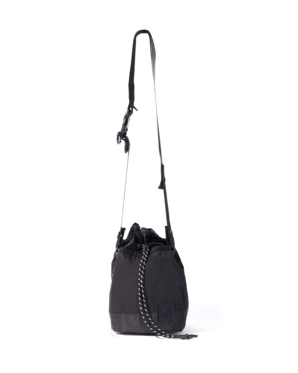 Straight suspended view of the black SYMA Sense Sling Bag hanging by its adjustable strap featuring a quick-release buckle and speckled paracord. Minimalist drawstring sling bag.