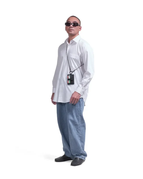 Full-body view of a male model in urban streetwear wearing the black SYMA Zipp around his neck, demonstrating its scale and card accessibility. Minimalist lanyard wallet.