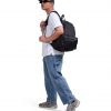 Full-body side view of a male model in urban streetwear wearing the black SYMA Foyer, demonstrating its large 21L scale and ergonomic fit. 16 inch commuter backpack.