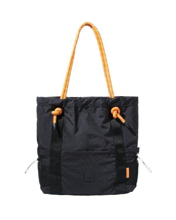Front vertical view of the 9L black SYMA Noble minimalist everyday tote bag, highlighting the nylon crinkle fabric, contrasting orange paracord shoulder straps, front vertical webbing, and dual external mesh water bottle pockets