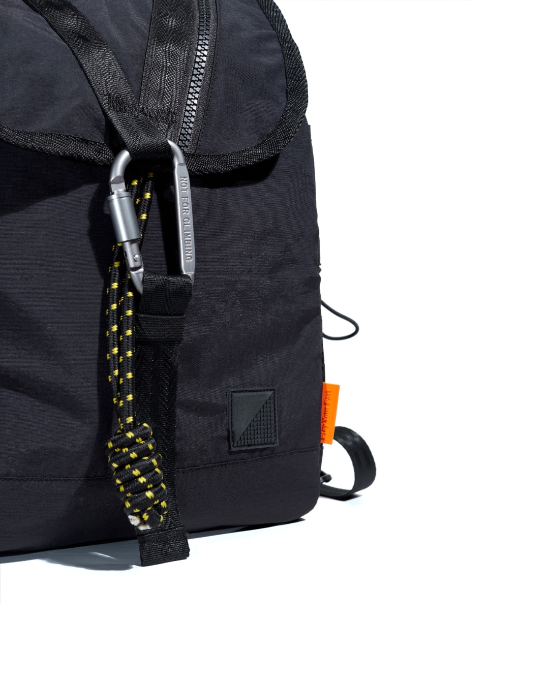 Extreme close-up of black SYMA Adore Backpack highlighting tactical carabiner, paracord, and orange signature tag. Compact everyday backpack