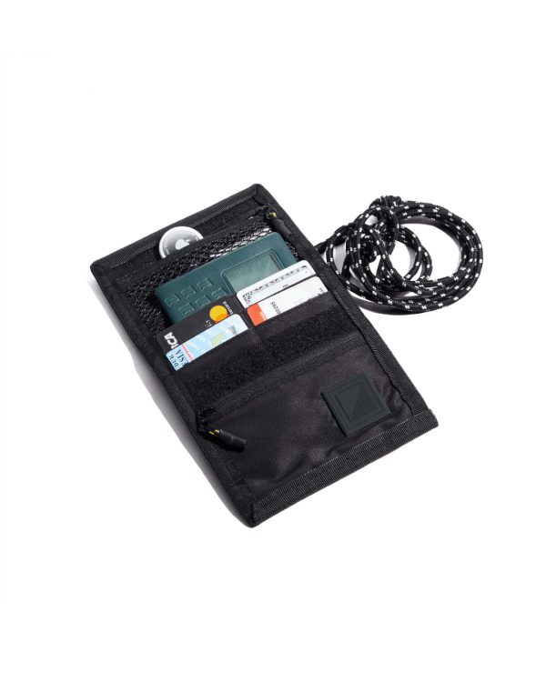 Top-down open view of the black SYMA Arrival compact travel wallet displaying organized interior slots with credit cards, a passport, an Airtag in the top mesh pocket, and attached paracord strap