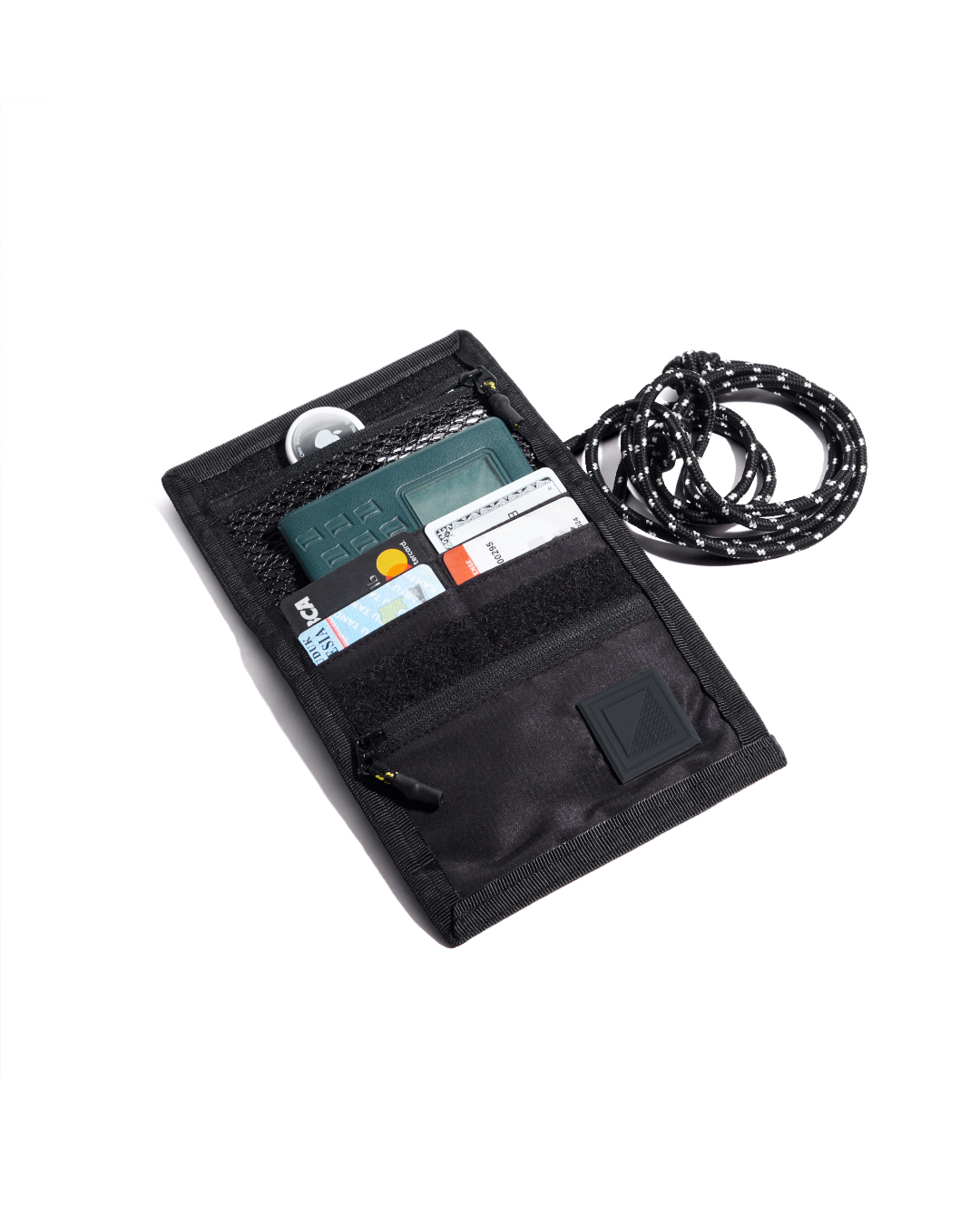 Top-down open view of the black SYMA Arrival compact travel wallet displaying organized interior slots with credit cards, a passport, an Airtag in the top mesh pocket, and attached paracord strap