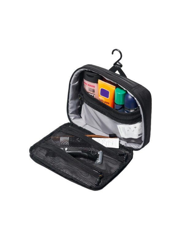 High-angle open interior view of the black SYMA Refine Toiletry Kit suspended by its built-in hook, demonstrating its organized compartments filled with grooming essentials like bottles and a razor inside zippered mesh pockets. Compact hanging toiletry bag.
