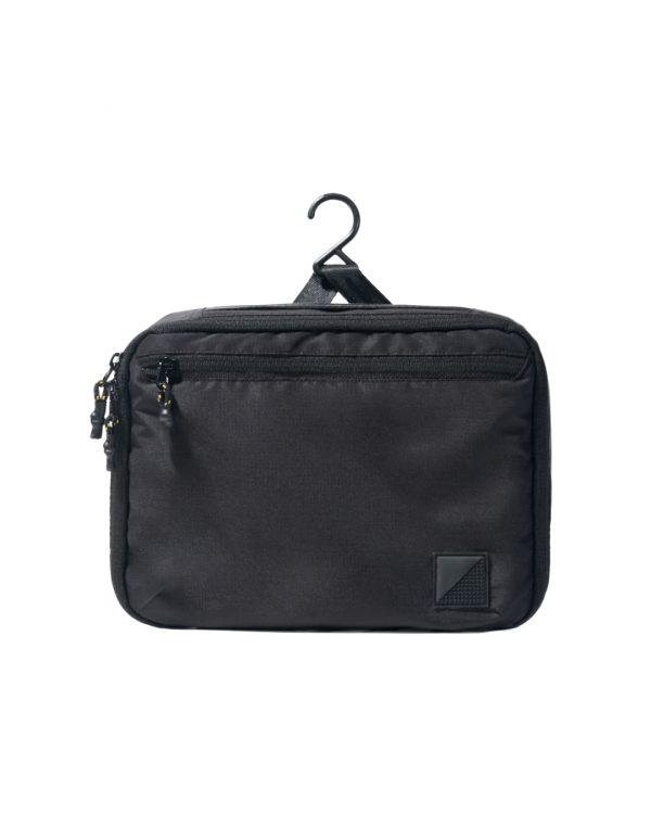 Straight suspended front view of the closed black SYMA Refine Toiletry Kit hanging by its built-in hook, highlighting its zippered front pocket and sleek exterior profile. Compact hanging toiletry bag.