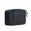 Closed three-quarter perspective view of the SYMA Refine Toiletry Kit in black, showcasing its water-resistant nylon exterior, quick-access front zipper pocket with blue paracord puller, main dual-zipper closure, and embossed black SYMA logo tag