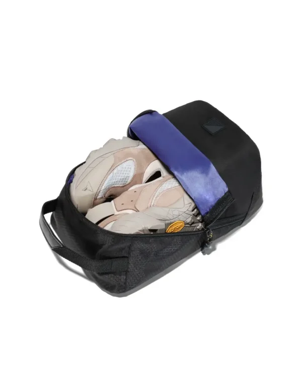 High-angle view of an open black SYMA Cubic showing a pair of beige sneakers inside its bright blue interior compartment. Ventilated travel shoe bag.