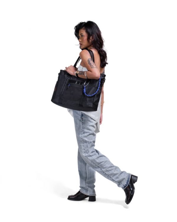 Woman in urban smart-casual attire carrying black SYMA Miles Tote Bag on shoulder. 16L versatile work tote bag
