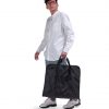 Male model in smart casual attire carrying the folded black SYMA Motion by its top handles, demonstrating its easy portability. Travel garment bag.