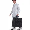 Male model in smart casual attire carrying the folded black SYMA Motion by its top handles, demonstrating its easy portability. Travel garment bag.