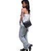 Full-body side view of a female model in casual streetwear wearing the black SYMA Strings Sling Bag, demonstrating its compact scale and front mesh pocket. Small urban crossbody bag.
