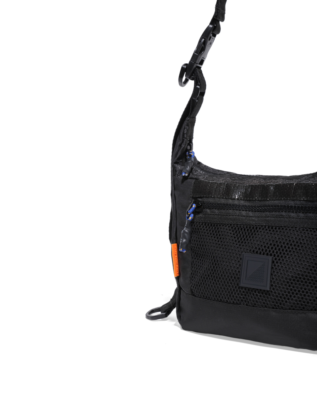 Close-up angled view of the black SYMA Strings Sling Bag highlighting its zippered front mesh pocket with speckled paracord pulls, glossy PE Tarpaulin panel, and signature orange side label. Small urban crossbody bag.