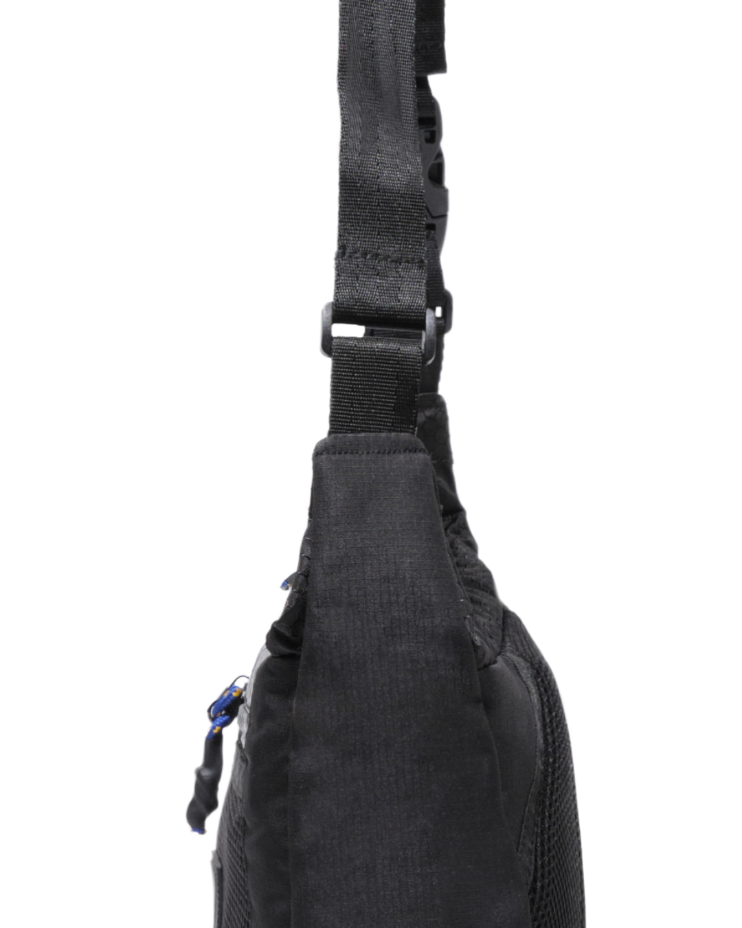 Close-up side profile of the black SYMA Strings Sling Bag highlighting its slim structured depth, heavy-duty strap attachment, and speckled paracord zipper pull. Small urban crossbody bag.