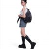 Full-body side view of a female model in Y2K-inspired streetwear wearing the black SYMA Symmetry Crossbody Bag, demonstrating its massive 19L capacity and ergonomic fit. Large techwear crossbody bag.