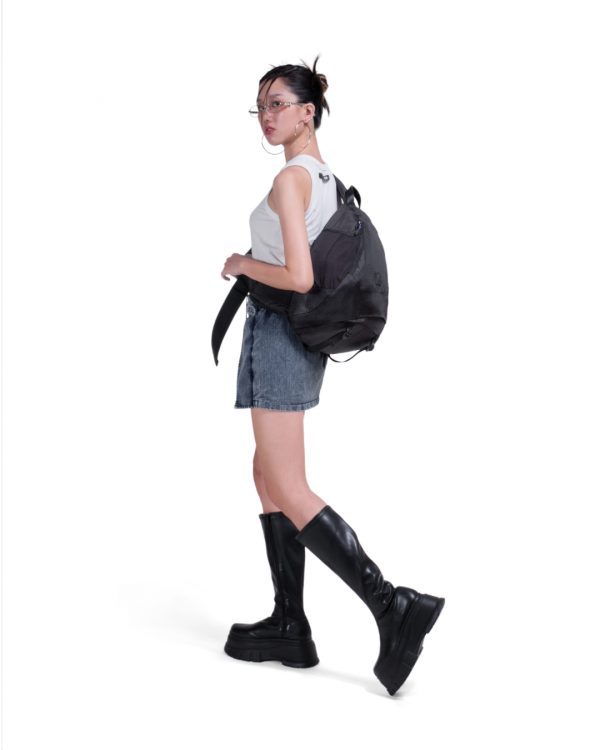 Full-body side view of a female model in Y2K-inspired streetwear wearing the black SYMA Symmetry Crossbody Bag, demonstrating its massive 19L capacity and ergonomic fit. Large techwear crossbody bag.