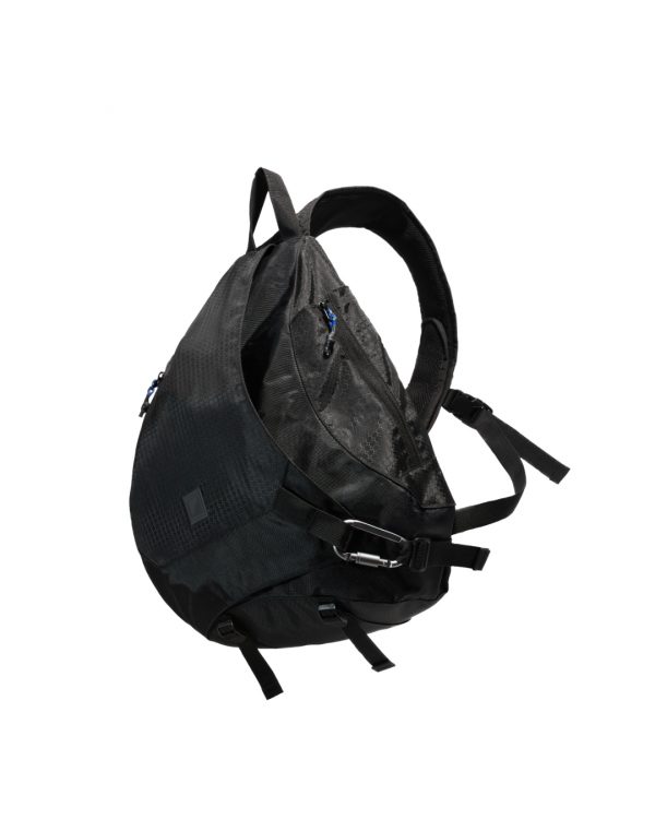 Angled suspended side view of the black SYMA Symmetry Crossbody Bag highlighting its ergonomic 19L silhouette, hexagon ripstop exterior, and heavy-duty metal carabiner lock. Large techwear crossbody bag.