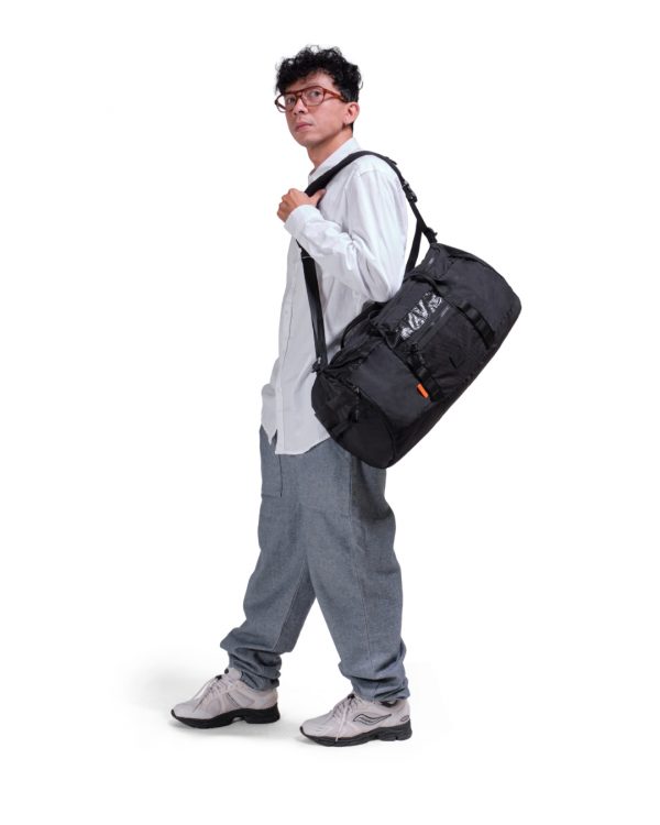 Man in athletic leisure attire walking while carrying the black SYMA Wonder Duffle Bag across his shoulder. A 38L versatile weekend duffle bag.