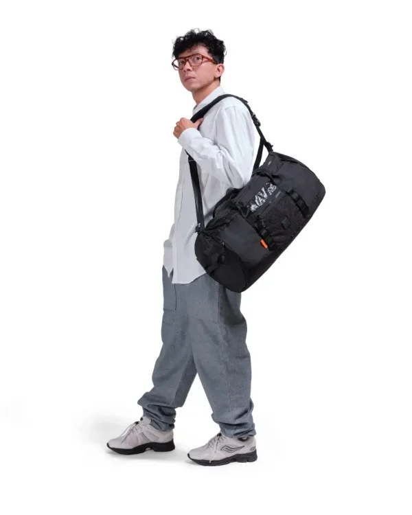 Man in athletic leisure attire walking while carrying the black SYMA Wonder Duffle Bag across his shoulder. A 38L versatile weekend duffle bag.