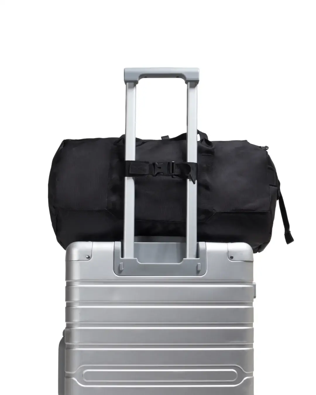 Demonstration of black SYMA Wonder Duffle Bag attached to silver suitcase handle using luggage strap. Versatile weekend duffle bag.