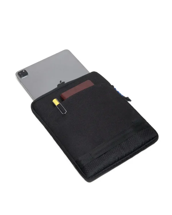 Angled top view of the black SYMA Opus with an iPad Pro partially inserted, highlighting its front pocket holding a notebook and pen. Tactical 11 inch tablet sleeve.