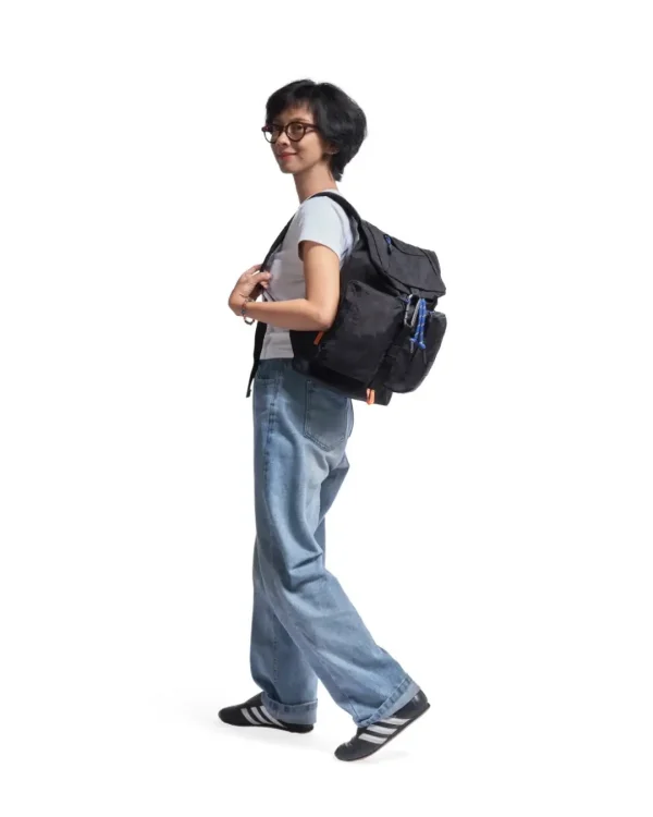 Woman in casual creative outfit walking with the black SYMA Ribbons Backpack over her shoulder. A 12L compact daily backpack.