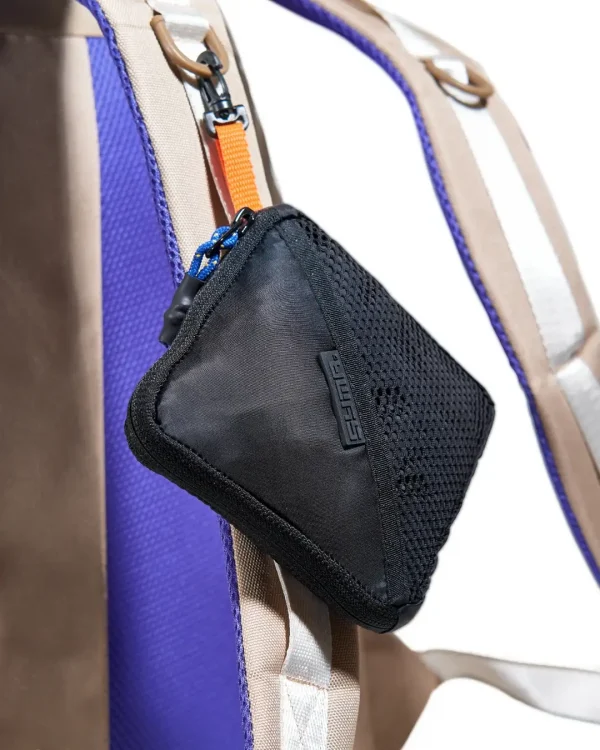 Close-up view of black SYMA Daytripper folded into its compact mesh pouch and attached to a backpack strap as a bag charm. Packable backpack rain cover