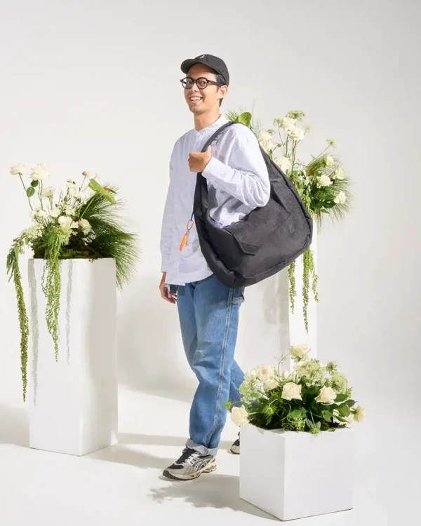 Man wearing SYMA Fable Sling Bag Black on shoulder. Oversized urban commuter messenger bag