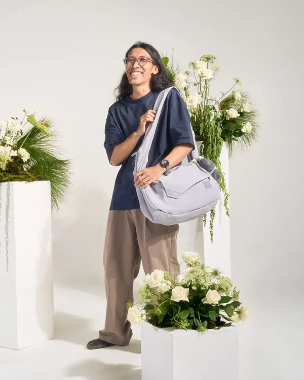 Man wearing SYMA Fable Sling Bag Light Grey on shoulder. 16L minimalist tech messenger
