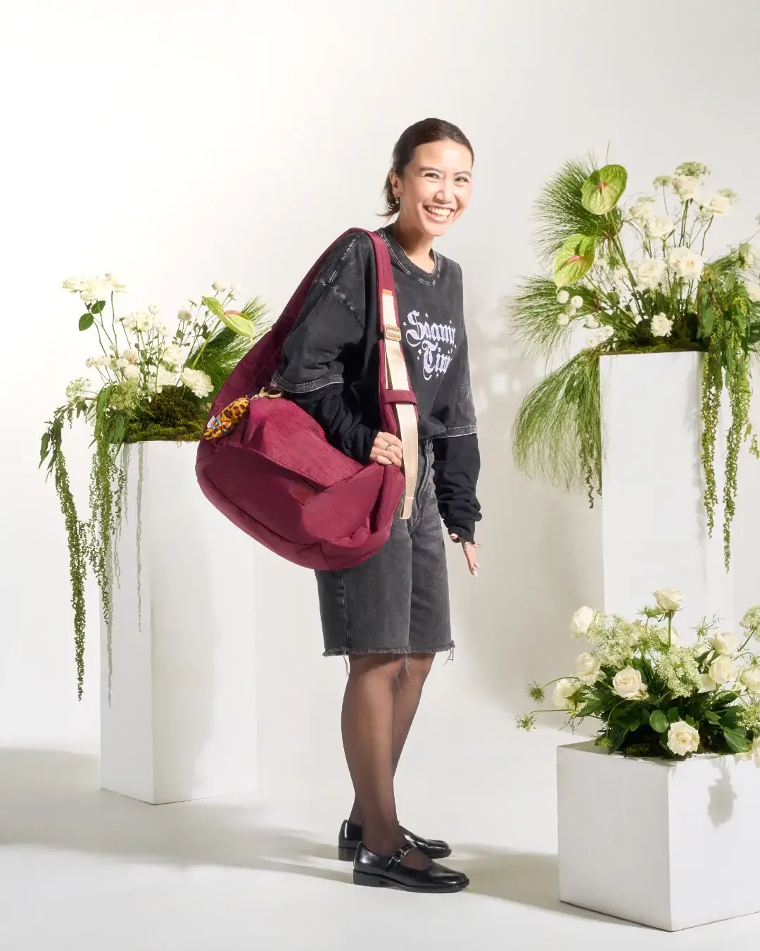 Smiling woman wearing SYMA Fable Sling Bag Maroon with oversized top. 16L urban streetwear sling bag
