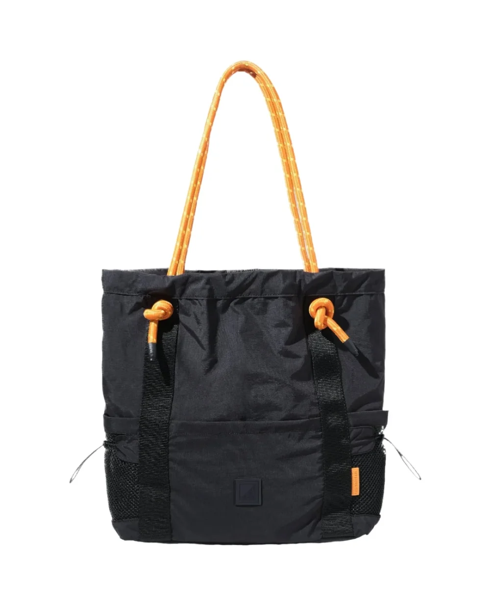 Front vertical view of the 9L black SYMA Noble minimalist everyday tote bag, highlighting the nylon crinkle fabric, contrasting orange paracord shoulder straps, front vertical webbing, and dual external mesh water bottle pockets