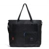 Straight front view of the SYMA Bridge Tote Bag in black, a premium urban utility tote featuring dual top handles, an adjustable crossbody strap, dual side mesh pockets, and a front compartment with a blue paracord YKK zipper puller