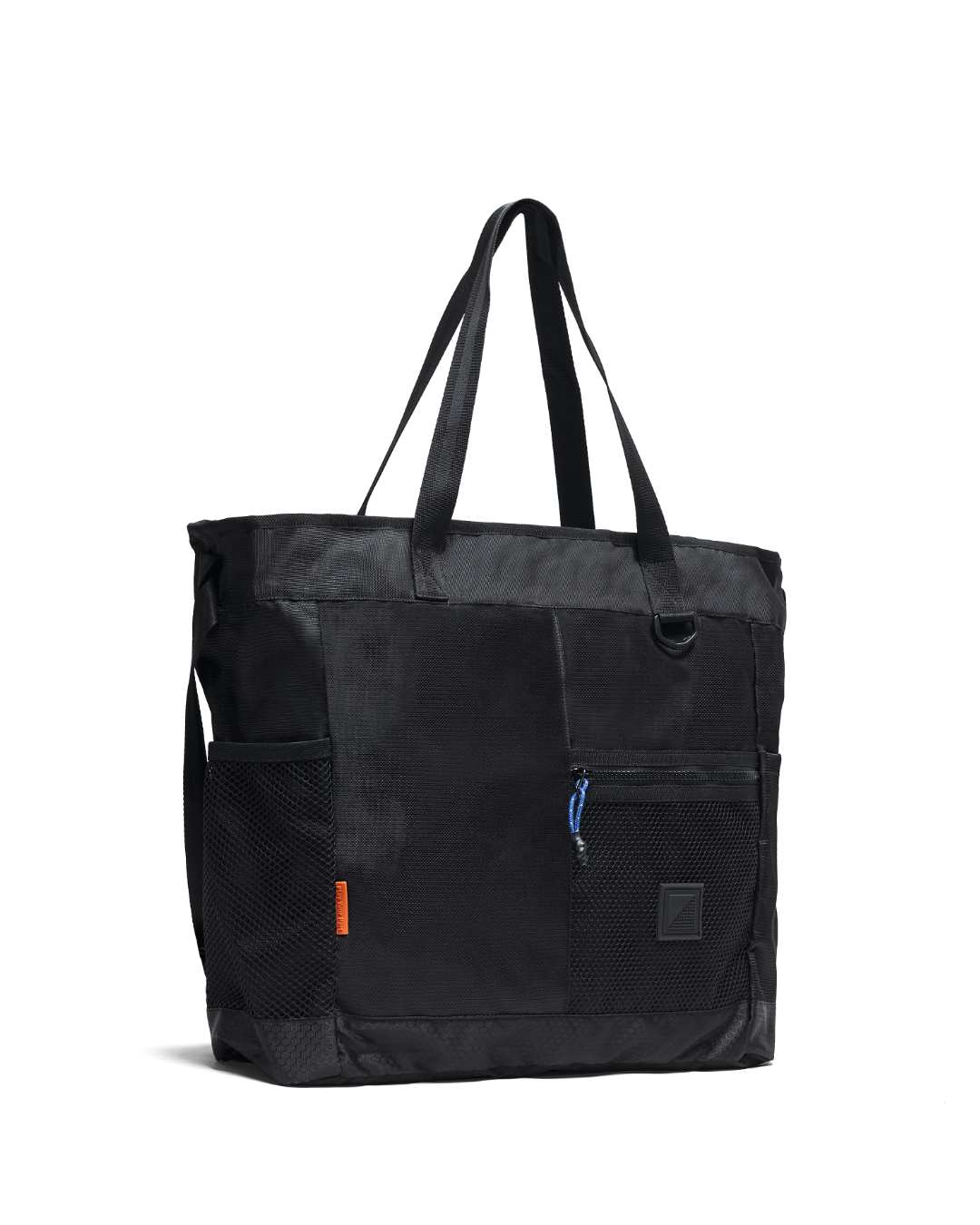 Three-quarter front view of the black SYMA Bridge Tote Bag, a premium urban utility tote featuring dual top shoulder straps, side mesh pockets with a small orange tag, a front zippered mesh compartment with a blue paracord puller, and a tonal black logo patch